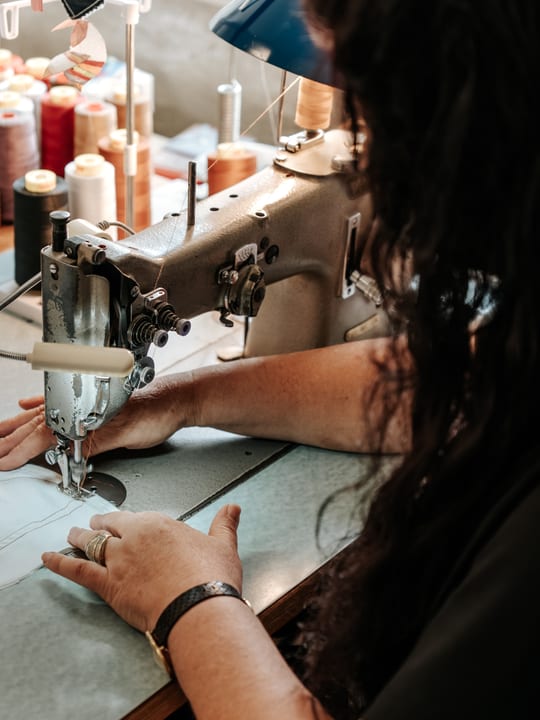 Näherin an einer Industrienähmaschine, im Hintergrund Garnrollen