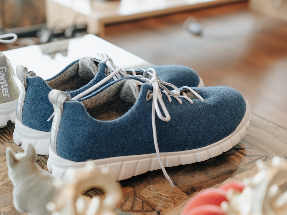 Produktfoto von blauen Filzsneakern mit weißer Sohle auf einem Holztisch