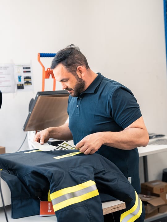 Mann arbeitet in einer Werkstatt an einer Einsatzjacke mit Reflexstreifen